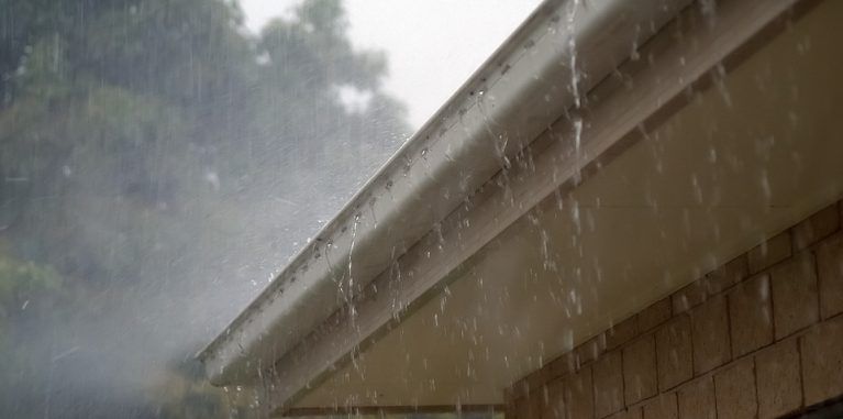 Rain pouring over the edge of a white residential gutter
